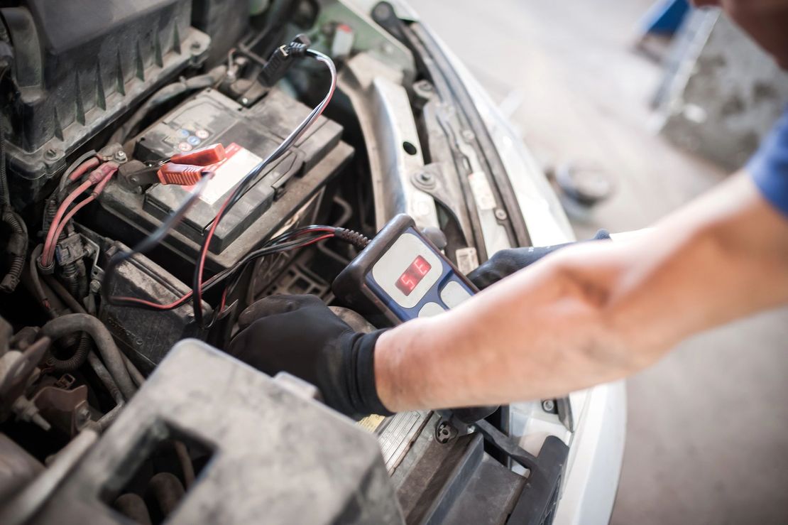 Un meccanico che controlla la batteria di un’auto con i cavi per l’avviamento in un’officina