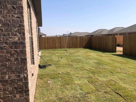 Backyard with green grass, wooden fence, and brick house wall along the left side