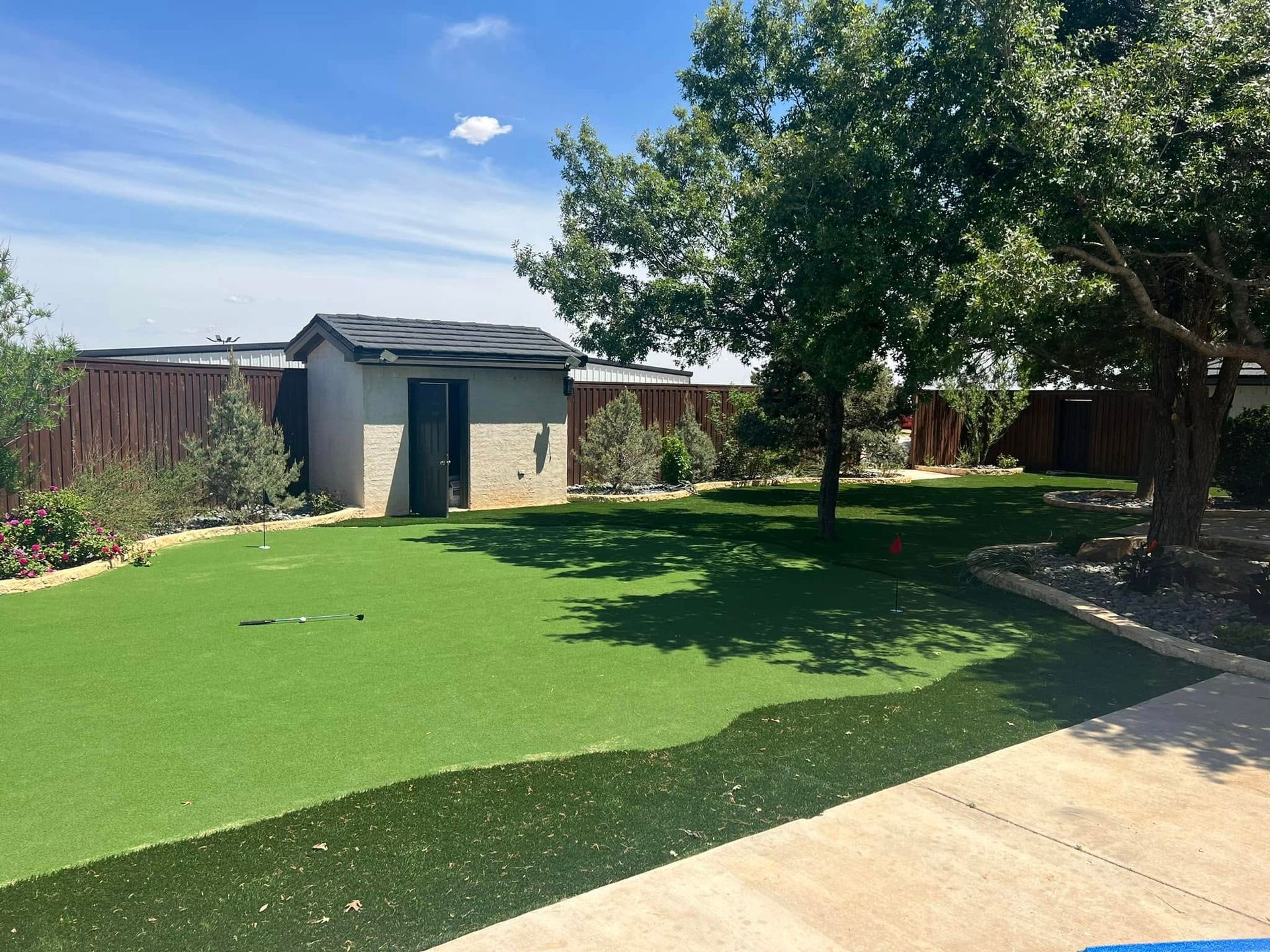 Backyard with artificial grass, patio, tree, and a small shed under a sunny blue sky