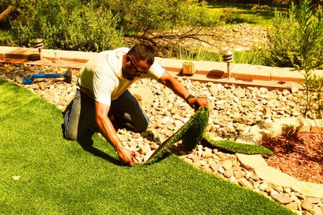 Man laying sod along a garden edge beside a rock bed and green lawn
