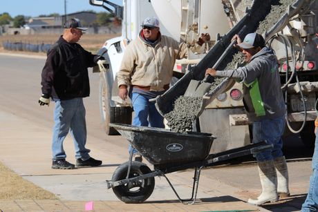 Construction crew pouring concrete with a wheelbarrow on a job site.