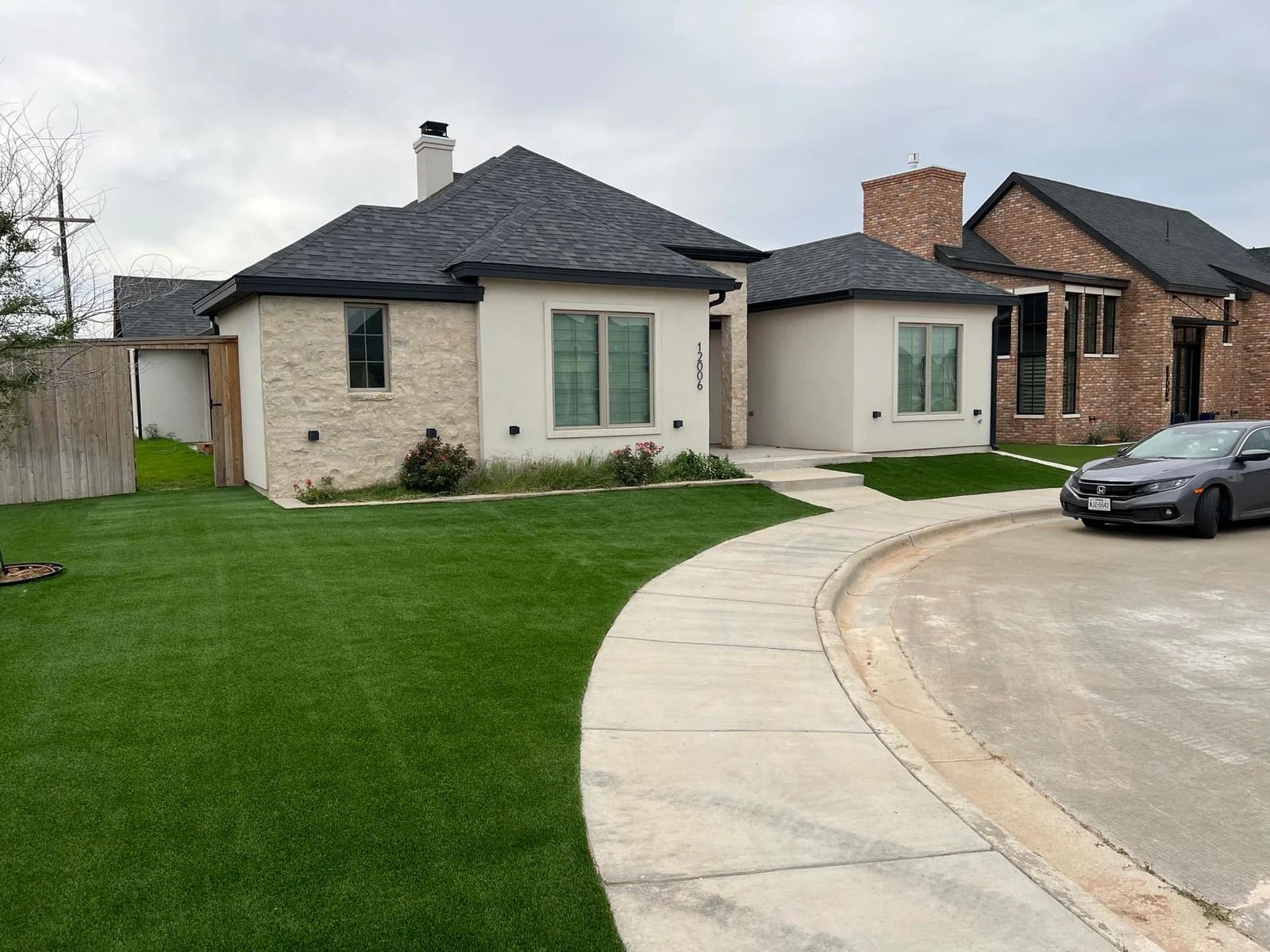Single-story suburban house with a green lawn, curved driveway, and parked car under a cloudy sky