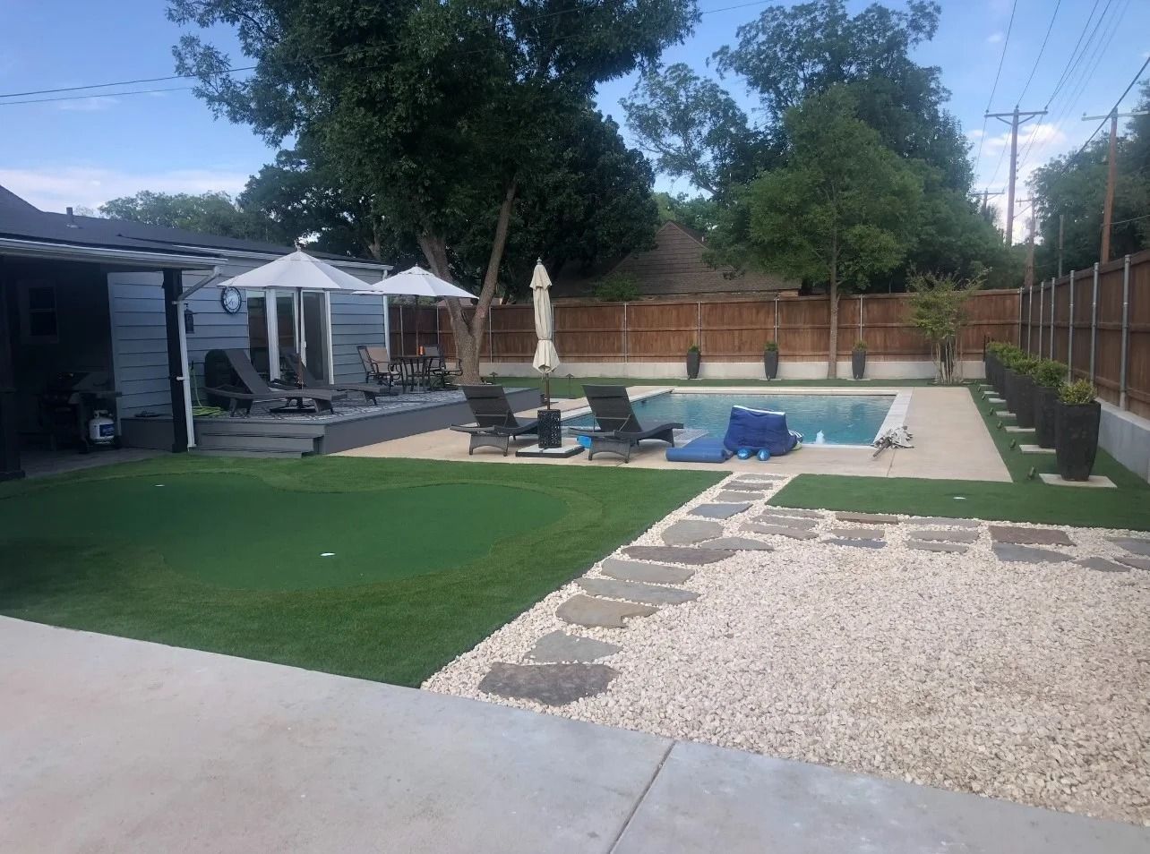 Backyard patio with pool, lounge chairs, umbrella, and artificial turf near a brick wall.