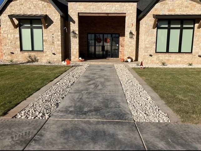 Front walkway leading to a stone house entrance with large windows and a double glass door.