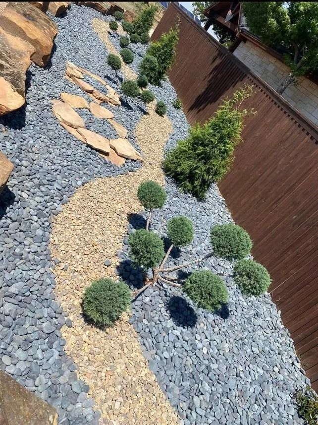 Landscaped yard with gravel, stepping stones, small shrubs, and a wooden fence along the side