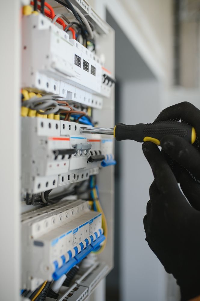 Gloved hand testing wires in an electrical control panel with circuit breakers