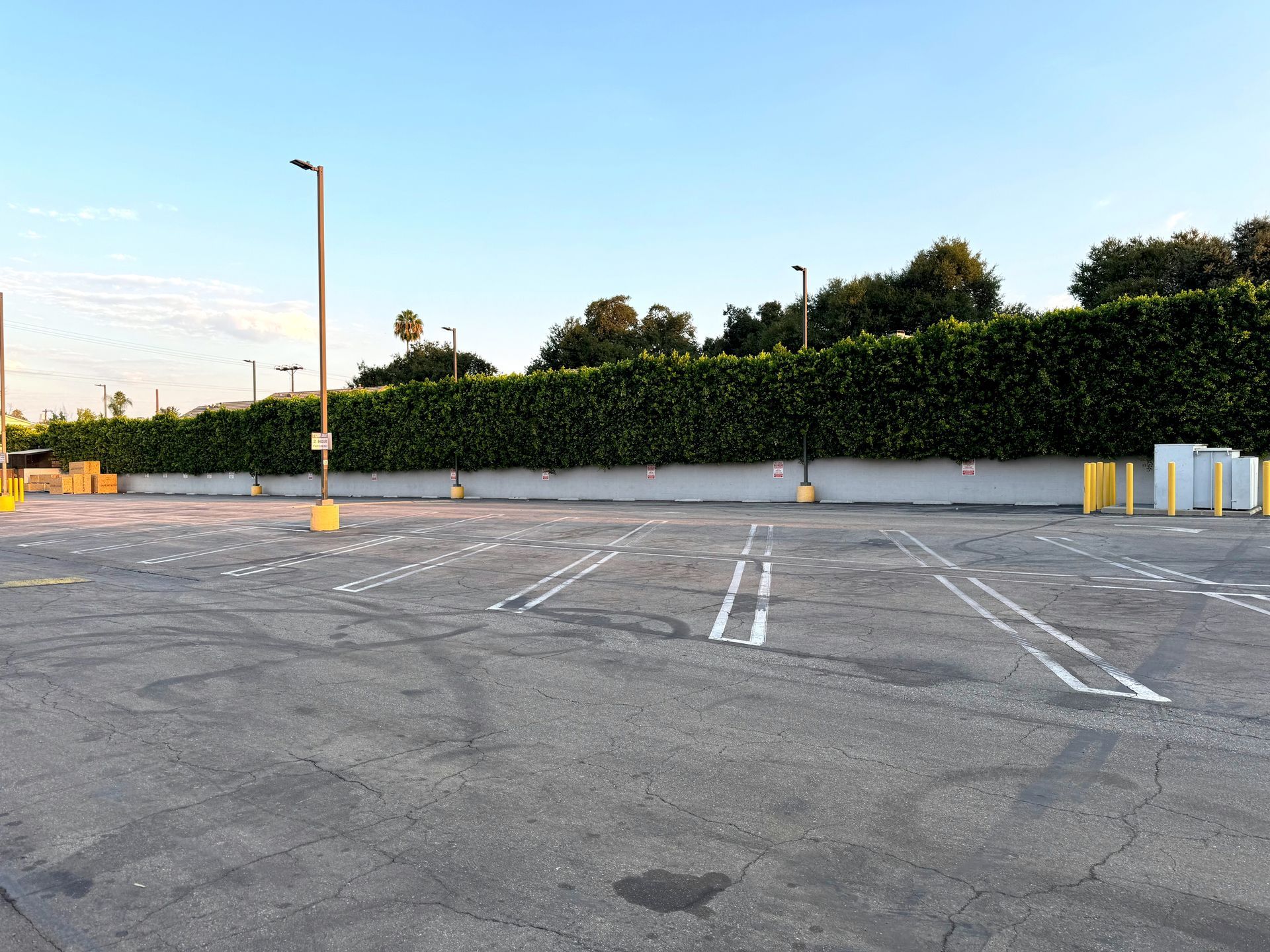 Empty parking lot with faded white lines, yellow bollards, and a hedge along the edge at sunset