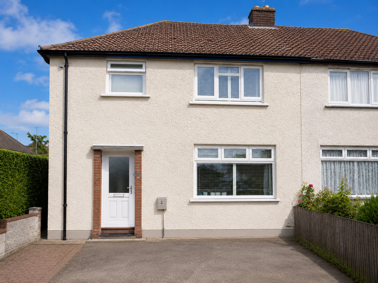 Semi-detached house with cream exterior, white door, and paved driveway under a blue sky