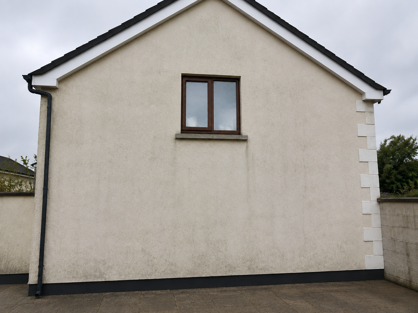 Back of a cream-colored house with a small brown-framed window and black base trim