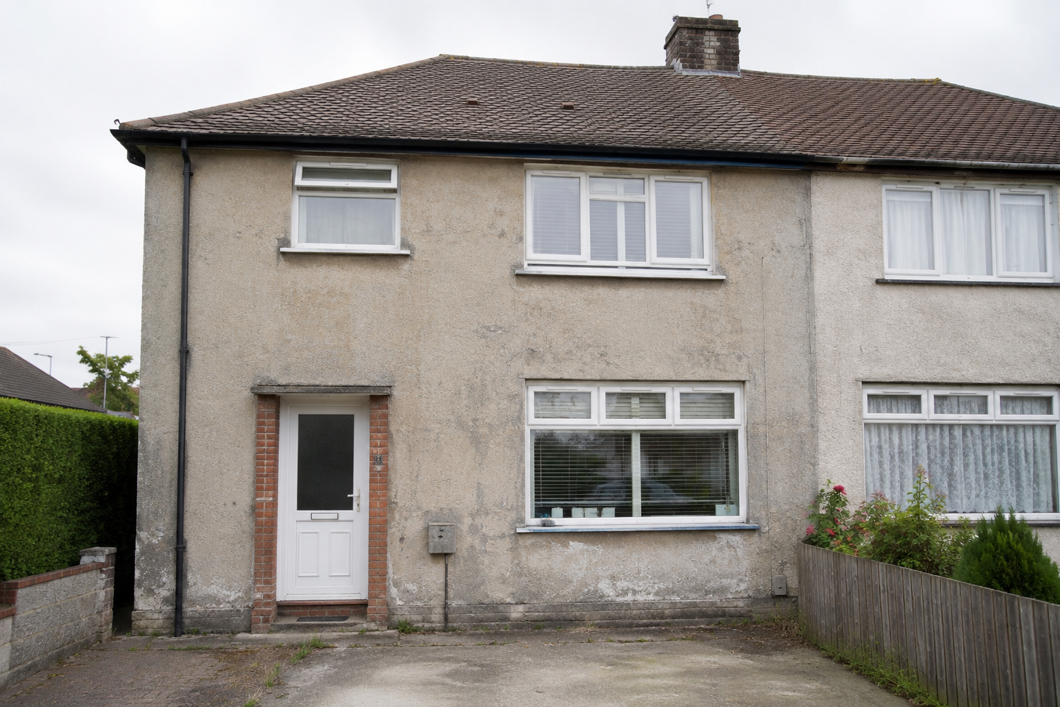 A small semi-detached house with a pebble-dash exterior, front door, and driveway.