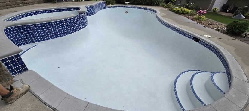 An empty, clean swimming pool with a tiled hot tub and curved steps, viewed from above.