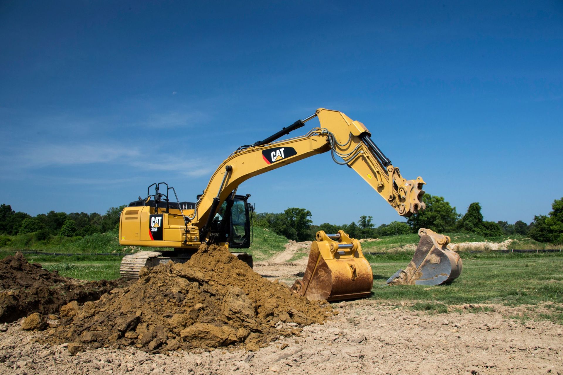 Yellow Caterpillar excavator digging in a field, under a blue sky.