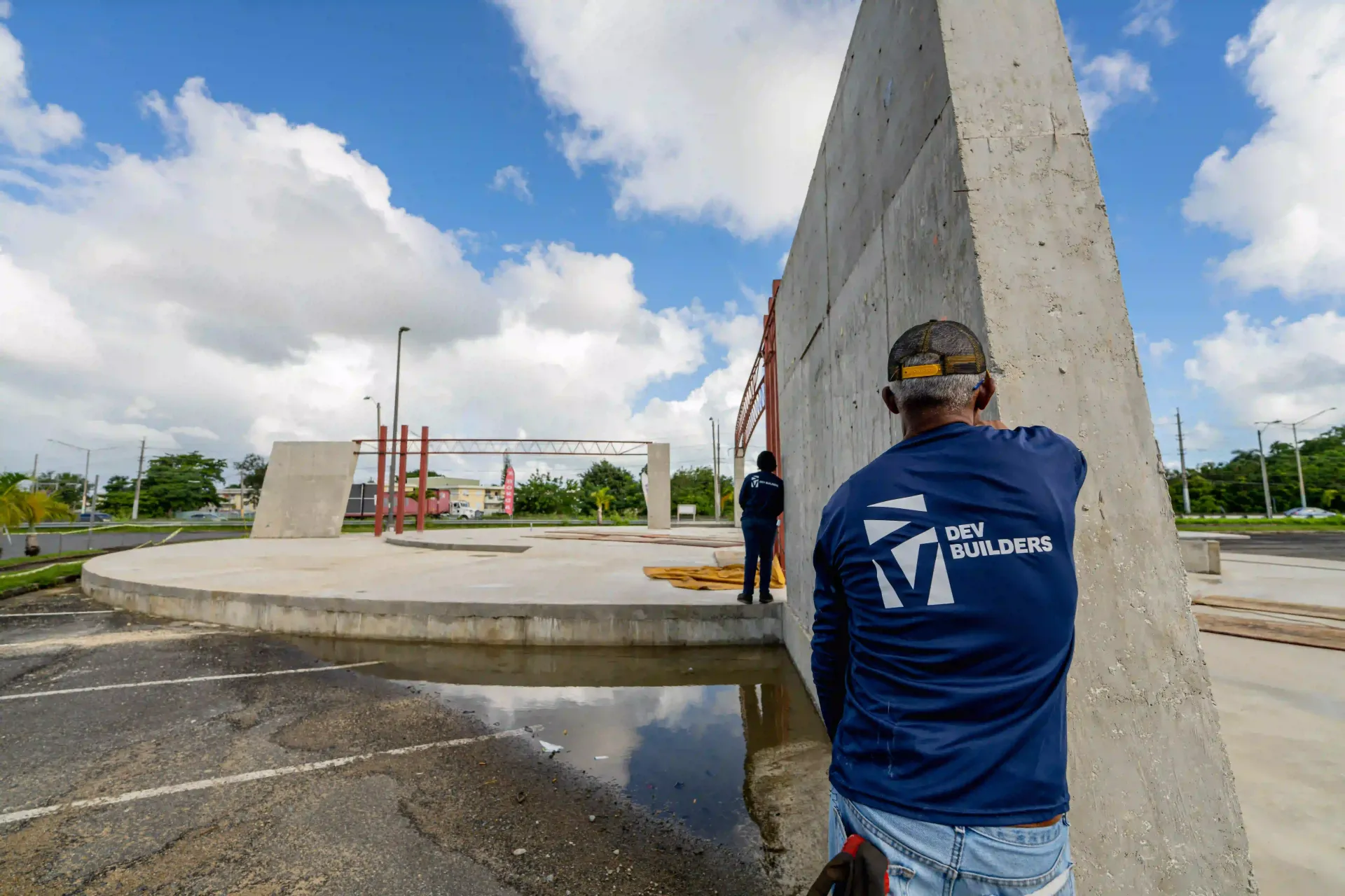 Person in blue shirt leaning on concrete wall at an outdoor construction site under a cloudy sky