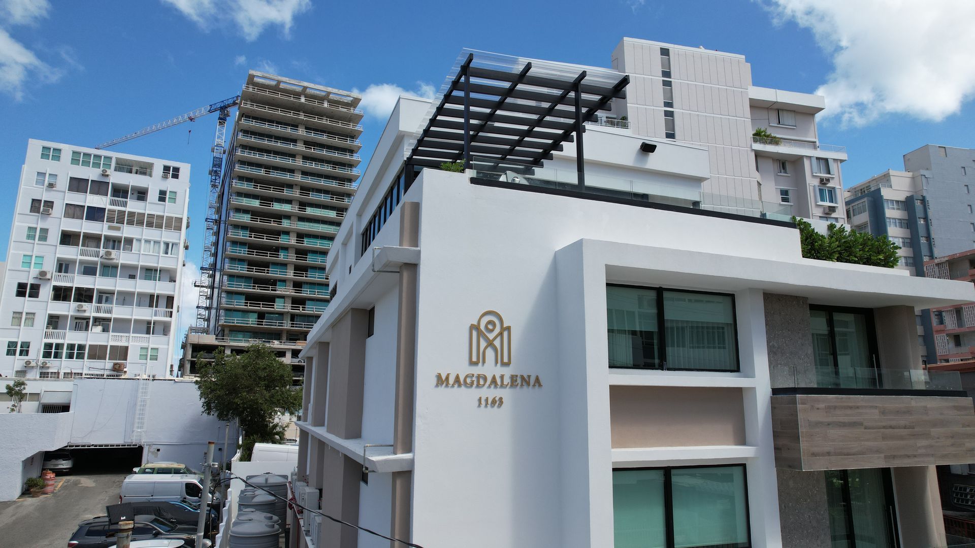 Modern hotel entrance with white facade and “Māgdalena” sign, city buildings in background