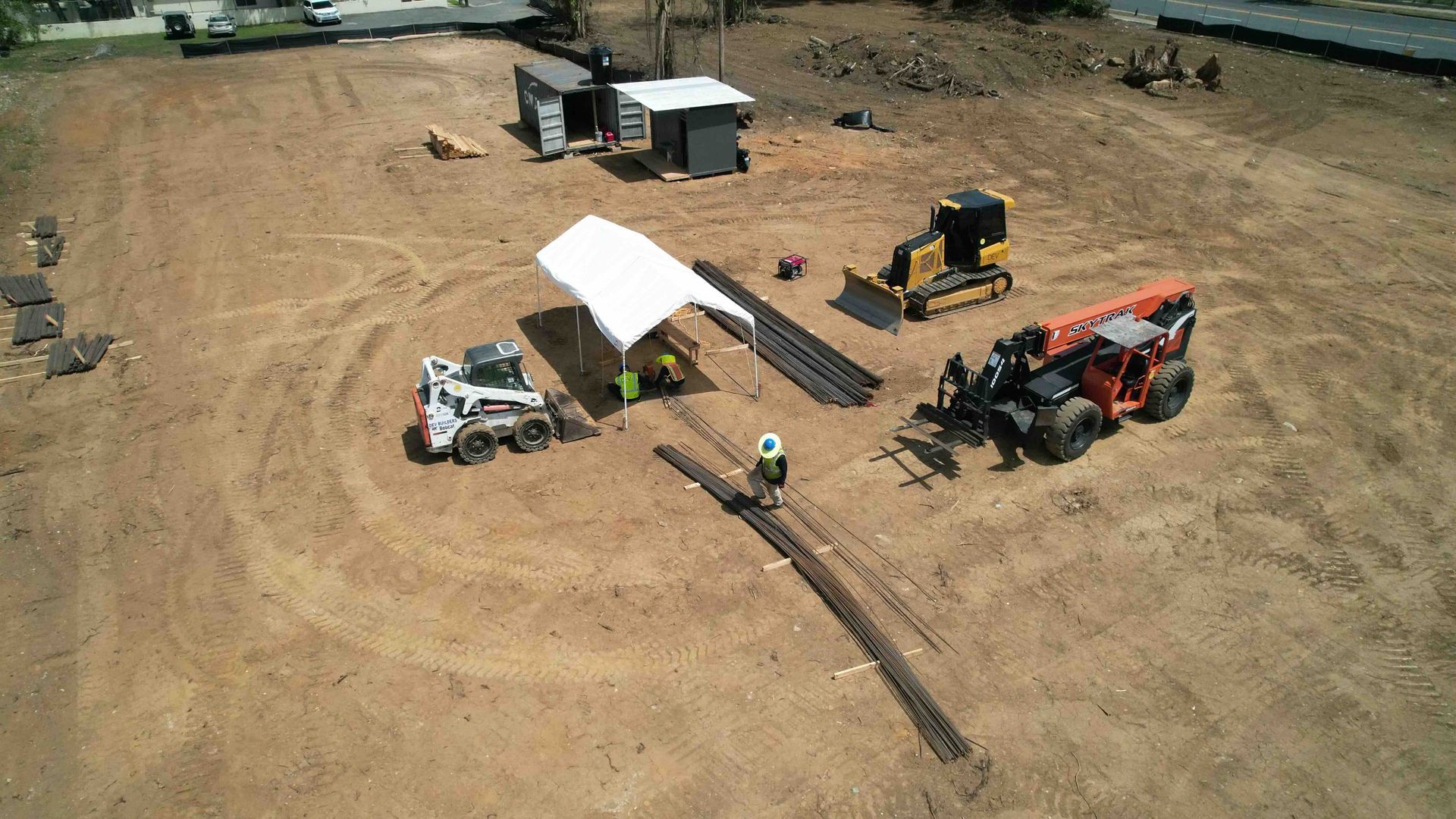 Construction site with excavators, a white canopy, trucks, and dirt grading work on a wide open lot
