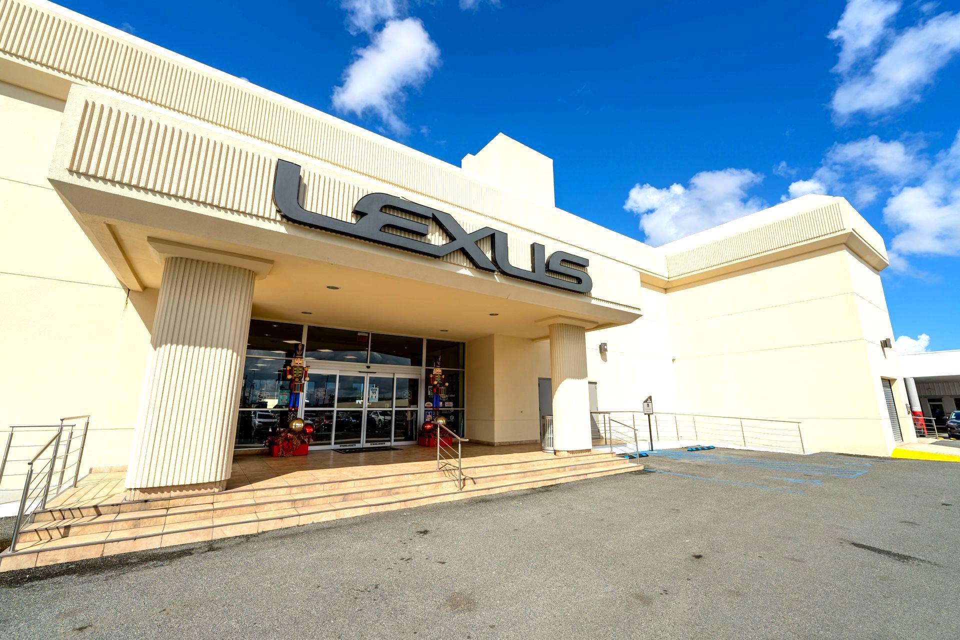 Exterior of a Lexus dealership with a glass entrance, beige facade, and blue sky overhead