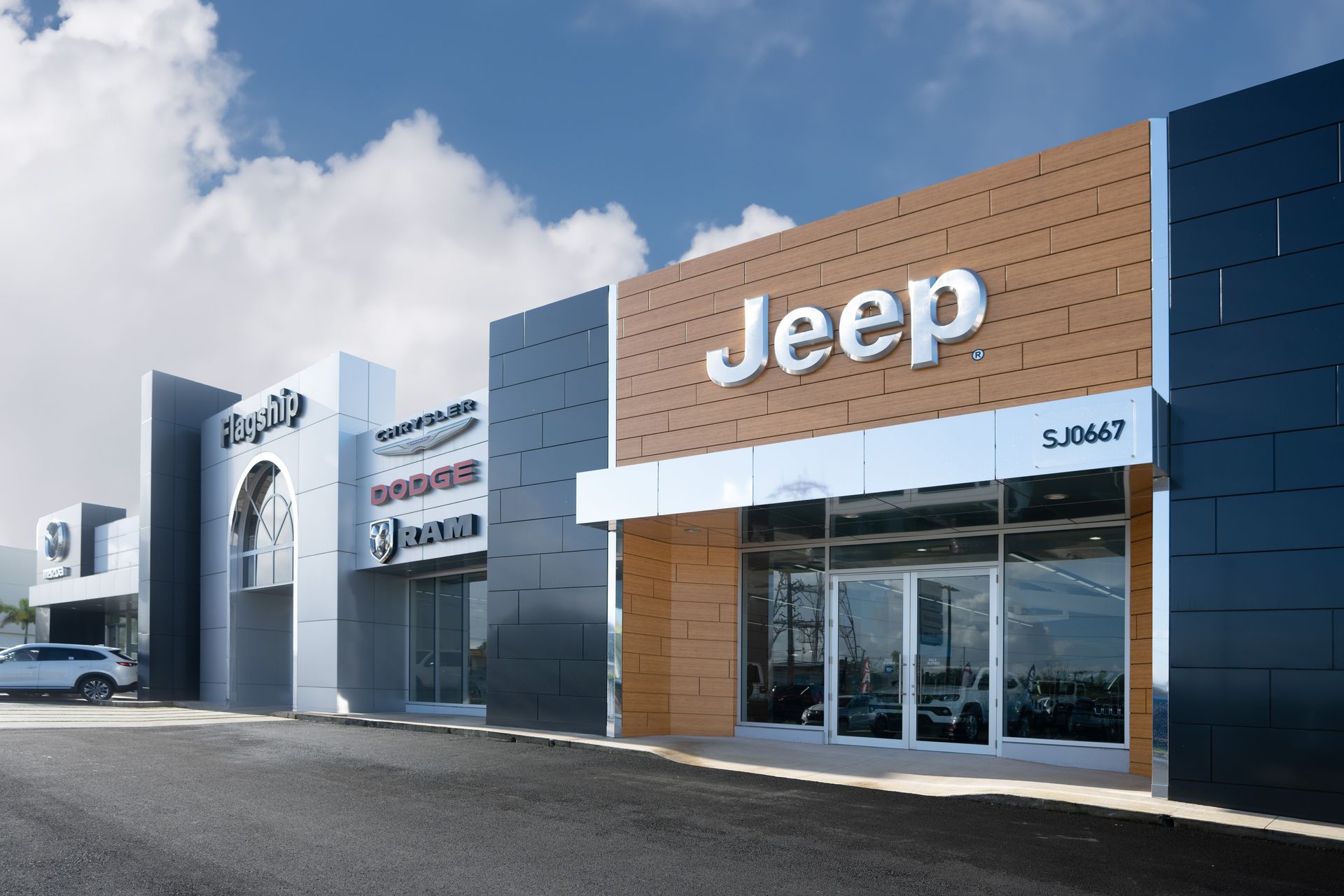 Jeep dealership exterior with modern showroom, large Jeep sign, and parked vehicles under a blue sky