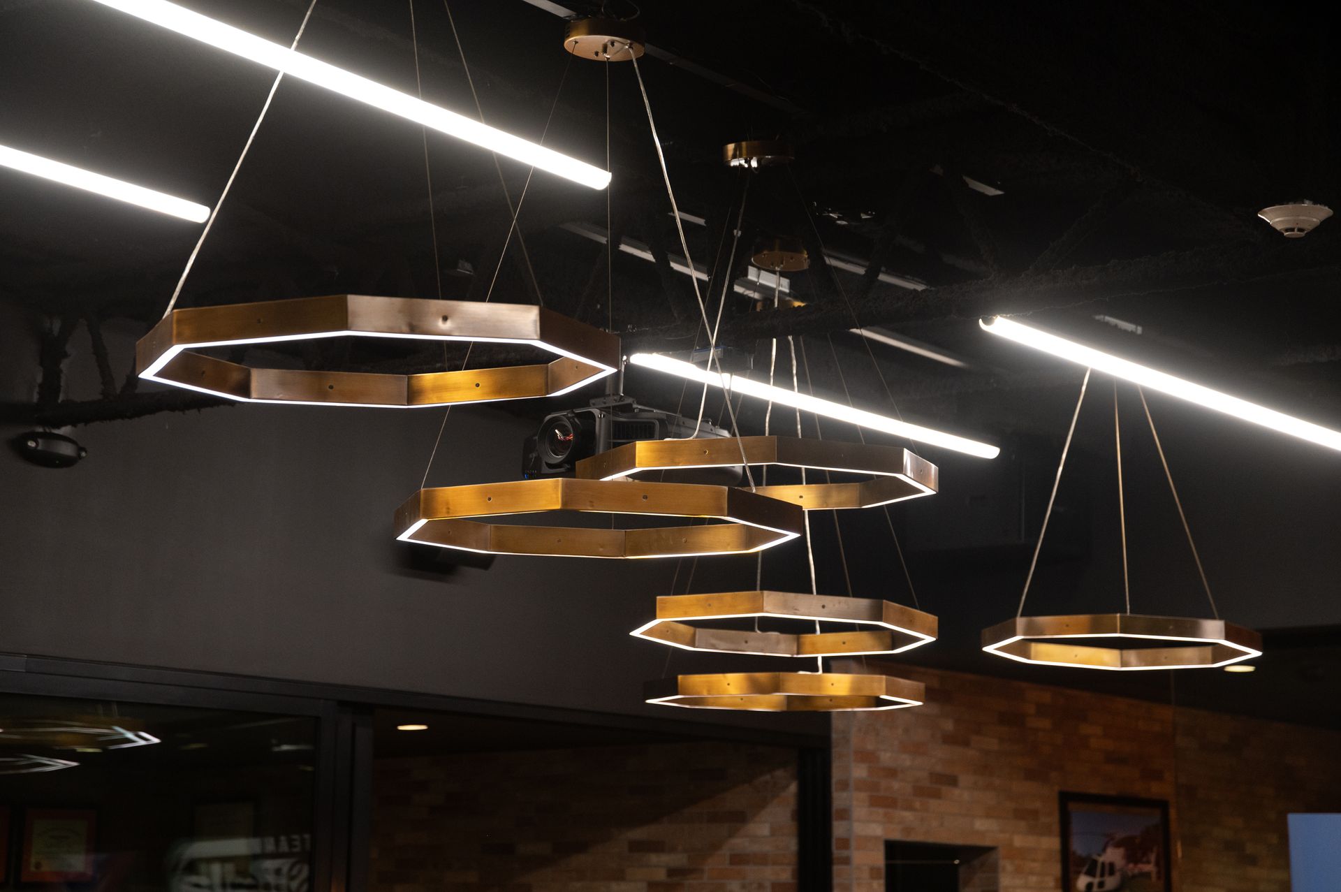 Several gold, hexagonal pendant lights hanging from a dark ceiling. Long white lights also in the ceiling all designed and built by DEV Builders.