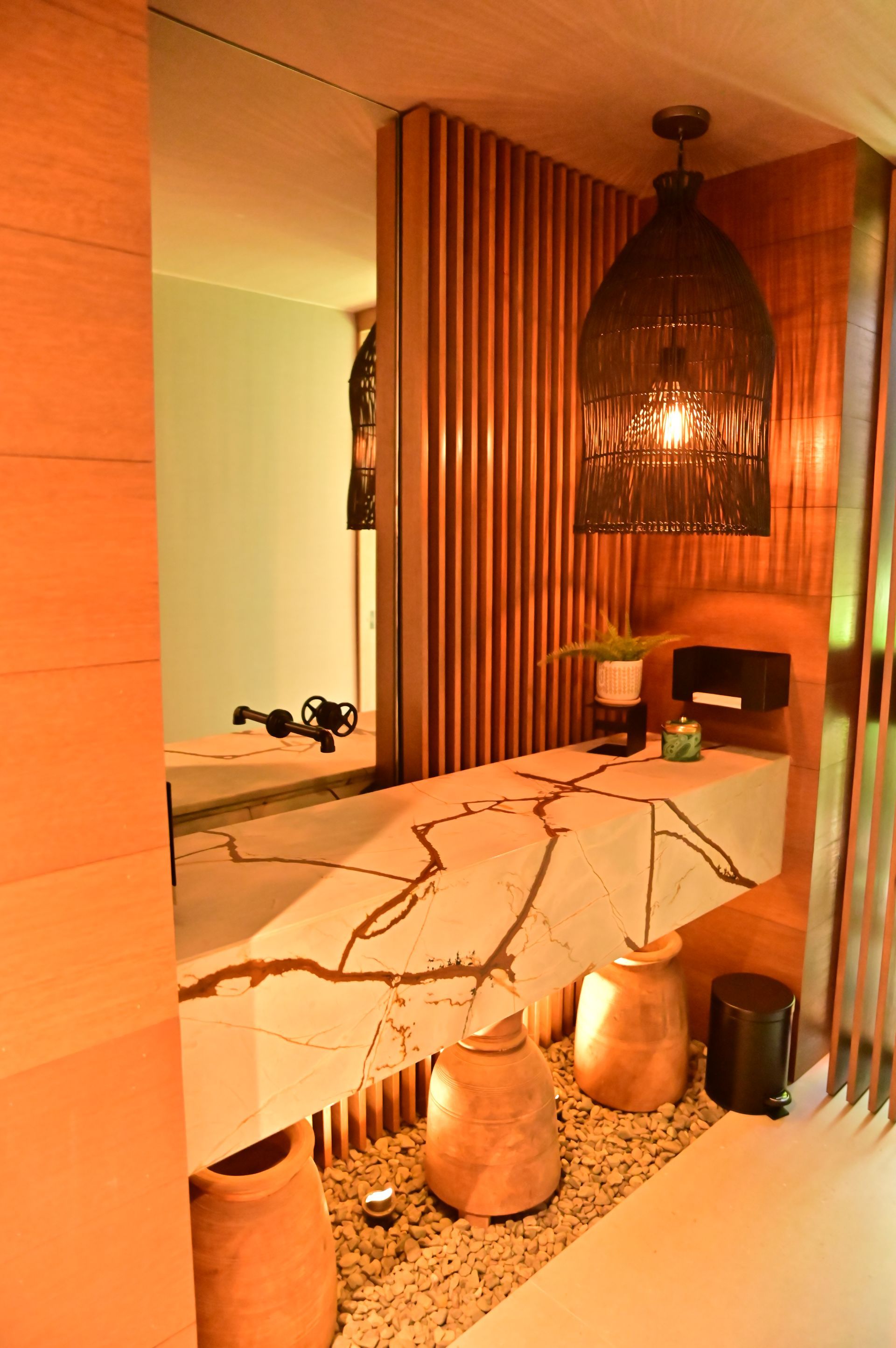Stylish spa room with marble table, woven chairs, pendant lamp, and warm wood slat walls