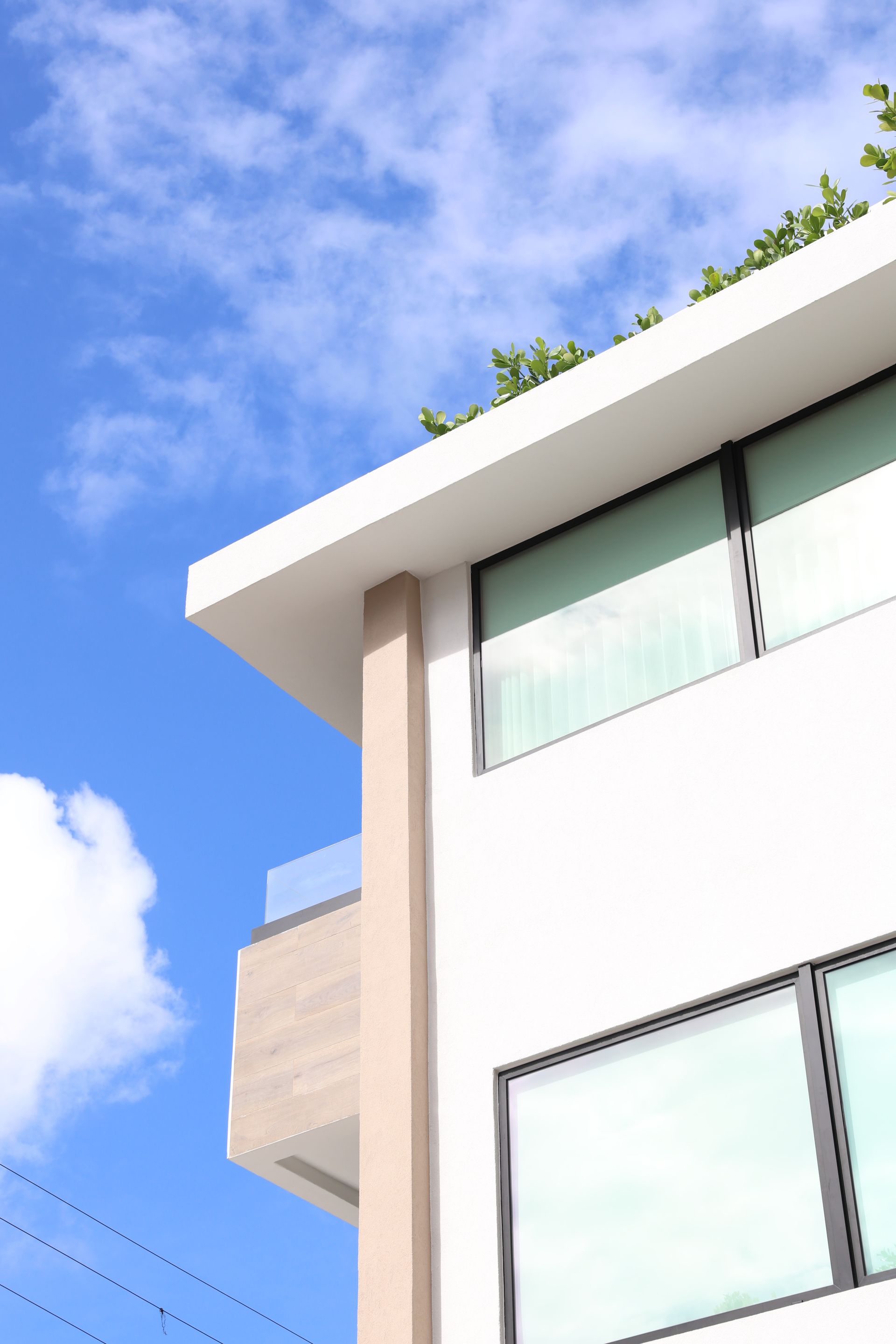 Modern white building corner with large windows against a blue sky and clouds