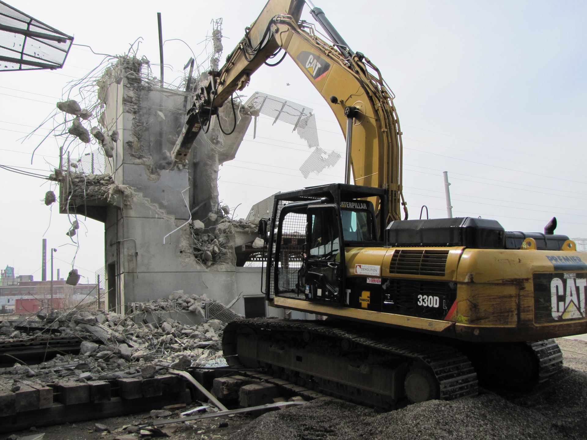 Yellow excavator demolishing a concrete structure, debris on the ground.