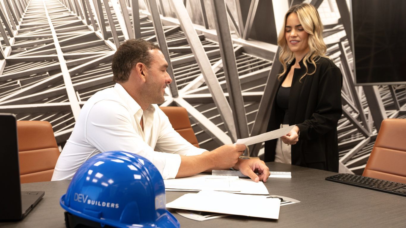 Business meeting with a man and woman shaking hands at a table, blue hard hat and papers in foreground