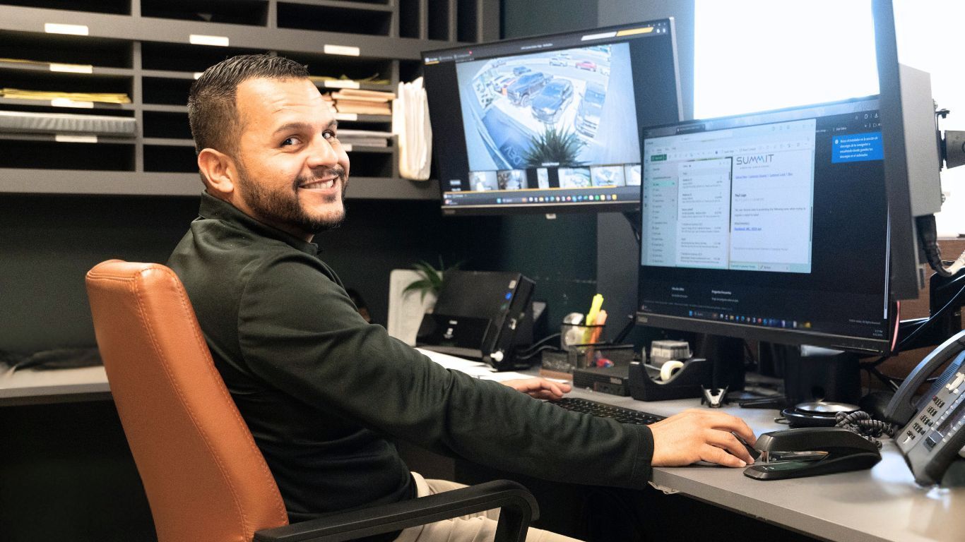 A man is sitting at a desk in front of two computer monitors.