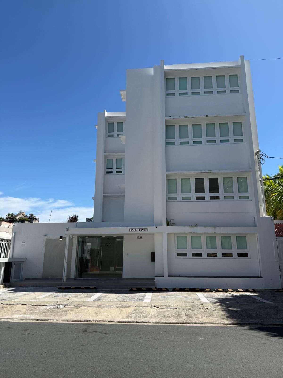 White four-story apartment building with glass windows under a clear blue sky
