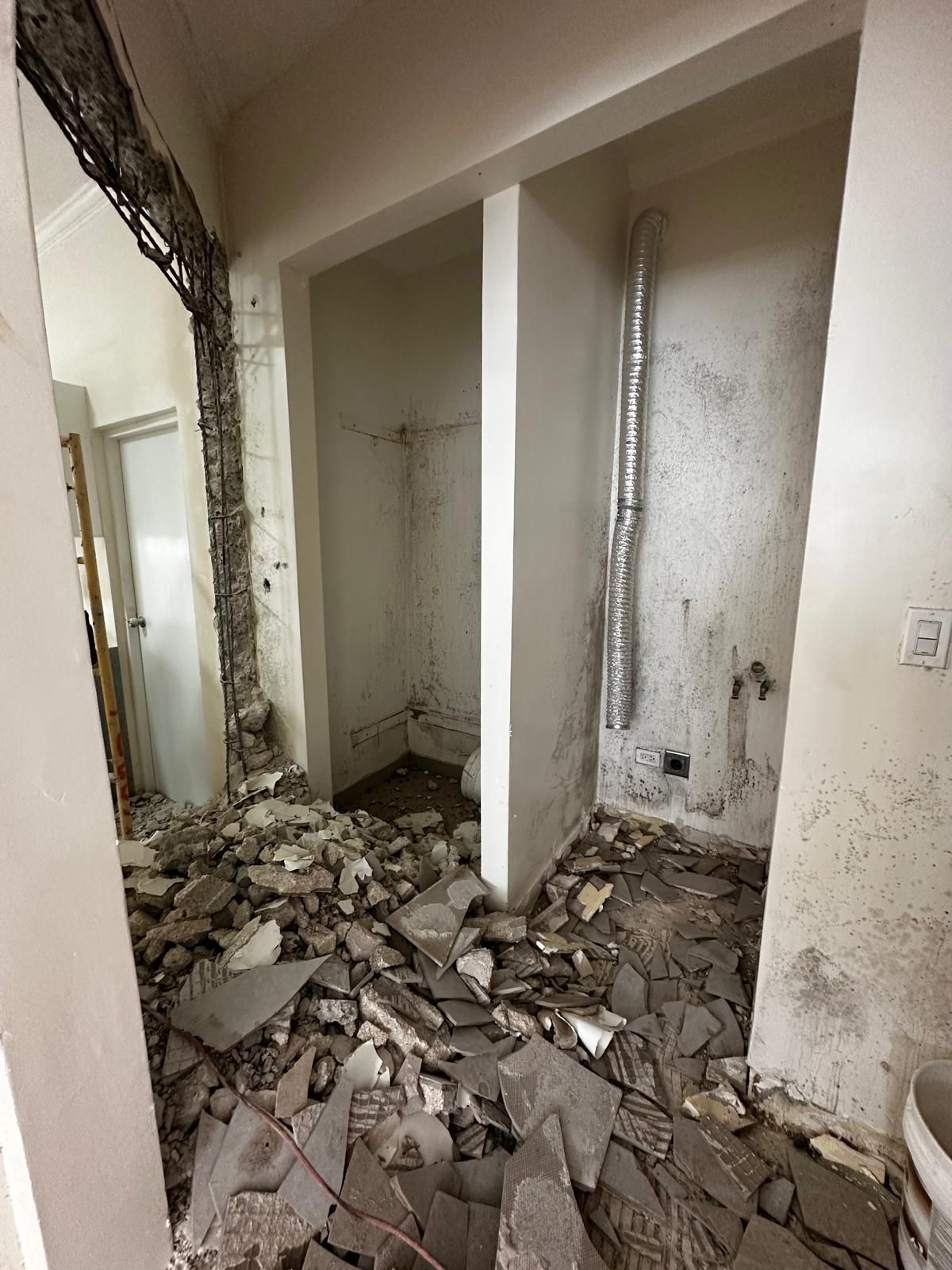 Interior demolition debris in a hallway, revealing a partially destroyed wall and a small room with a toilet.