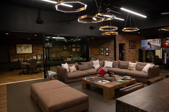 Lounge area with a brown sectional sofa, coffee table, and ottomans, next to an office with dark walls and decorative lighting in Puerto Rico.