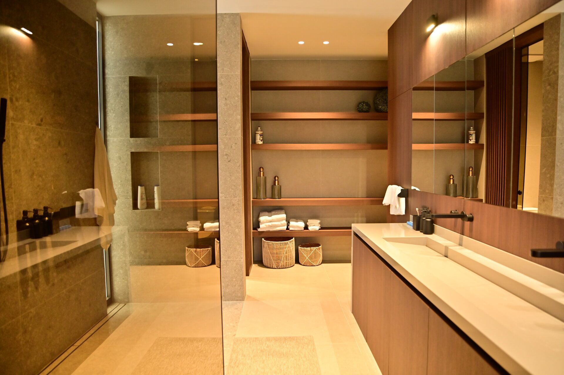 Modern bathroom with stone walls, wooden shelves, and a long sink counter.