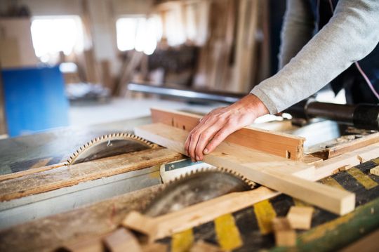 Person using a table saw to cut wood in a workshop.