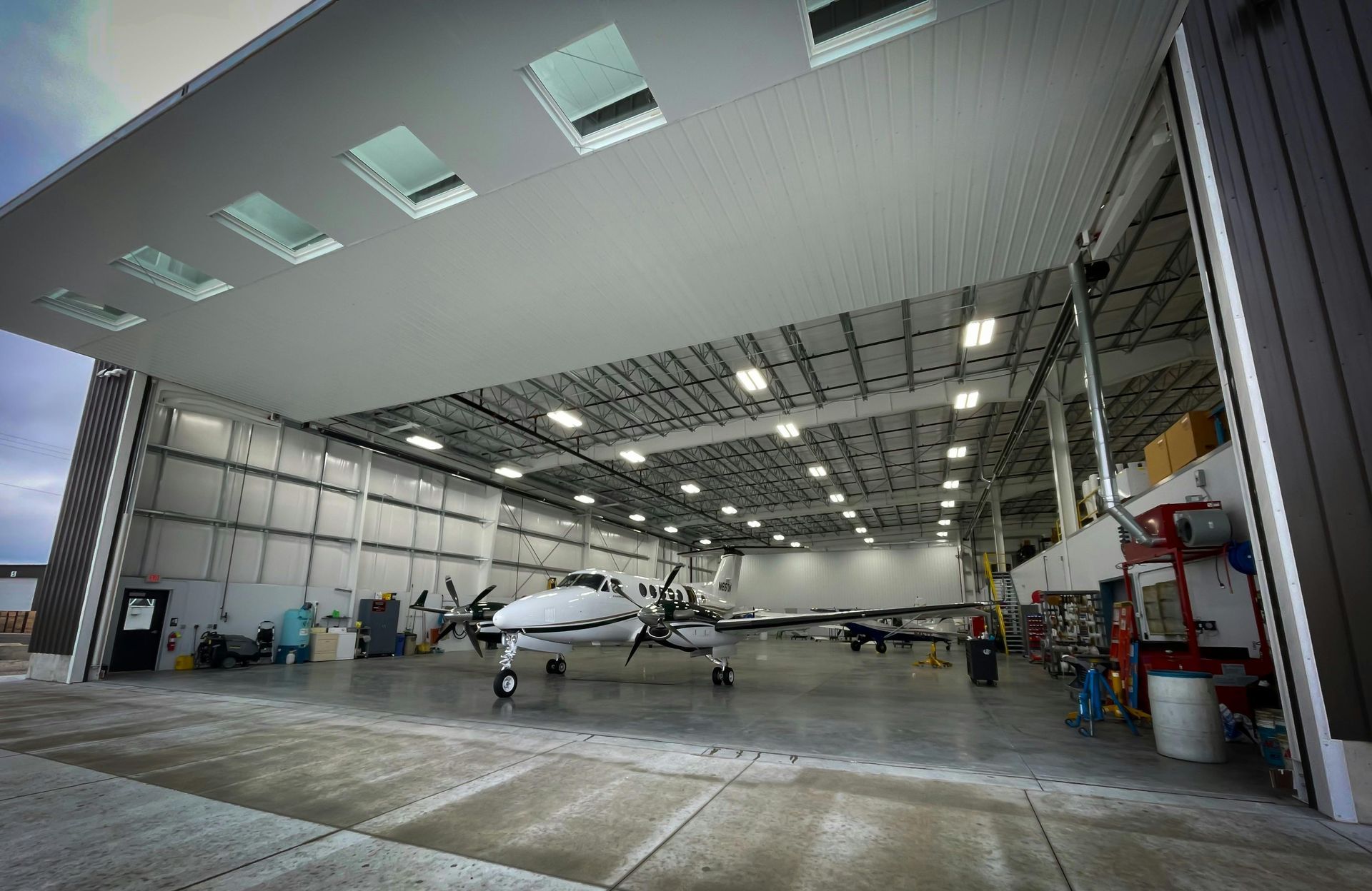 A small white propeller plane parked inside a large, high-ceilinged hangar with a wide, open door.