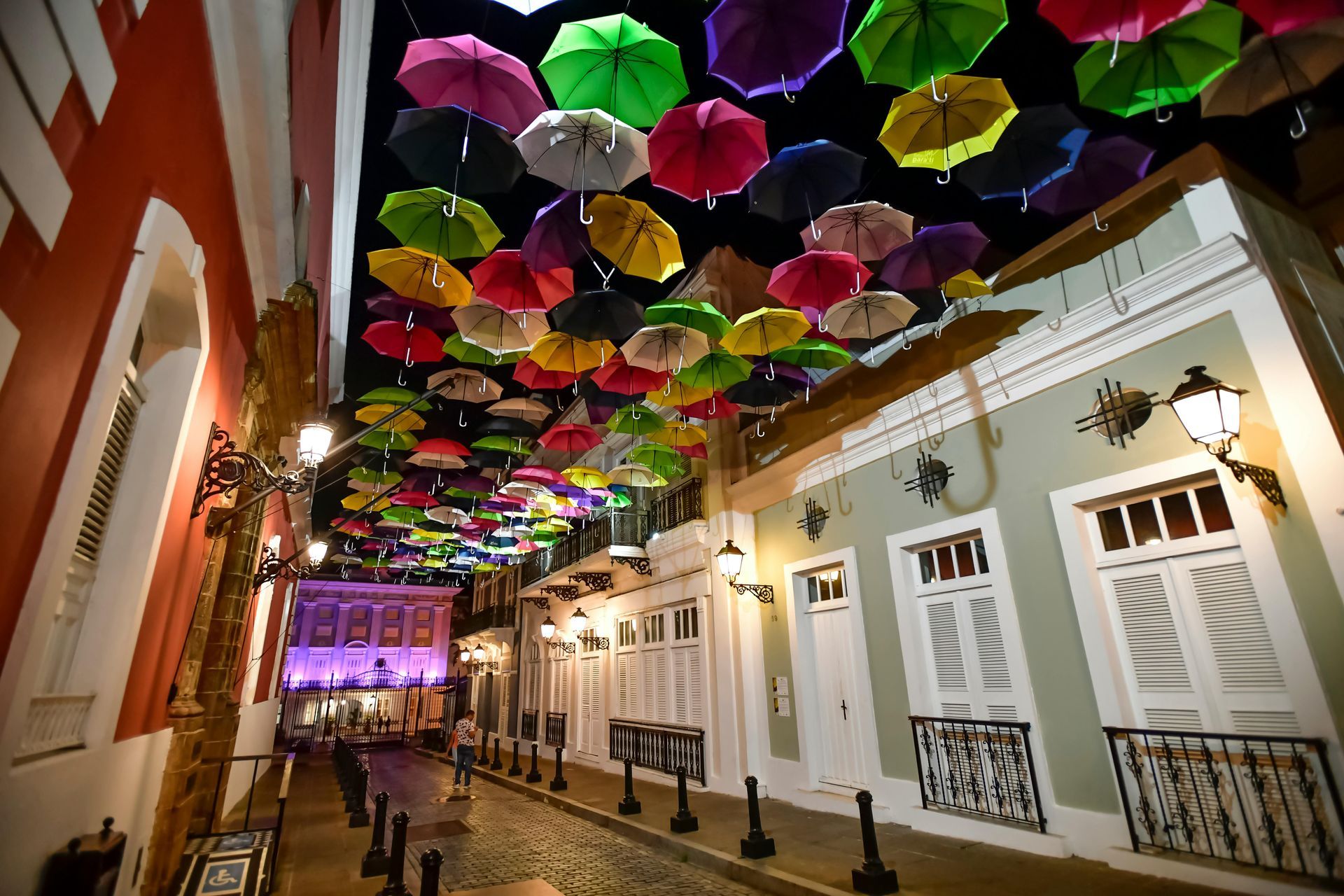 Night street with colorful umbrellas strung overhead above a narrow, lit alley of buildings