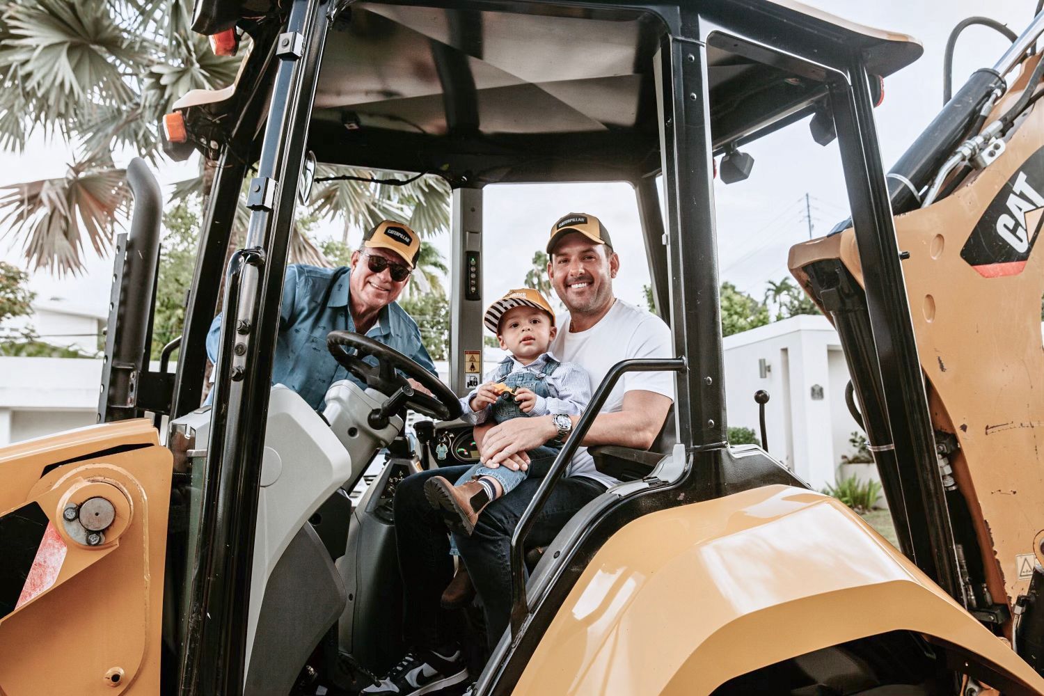 Three people in a yellow CAT tractor cab; two adults and a child. Smiles. Outdoors.