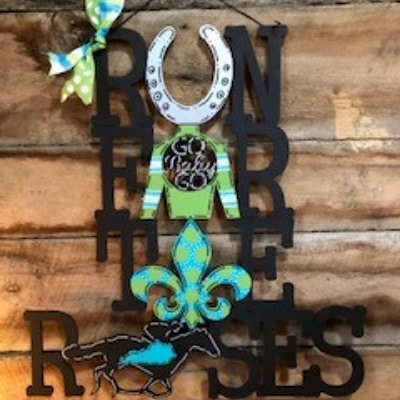 Decorative rustic wall art reading “Run for the Roses” with a horseshoe and blue-green fleur-de-lis accents
