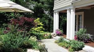 Garden path beside a house with white columns, lush greenery, and pink flowers