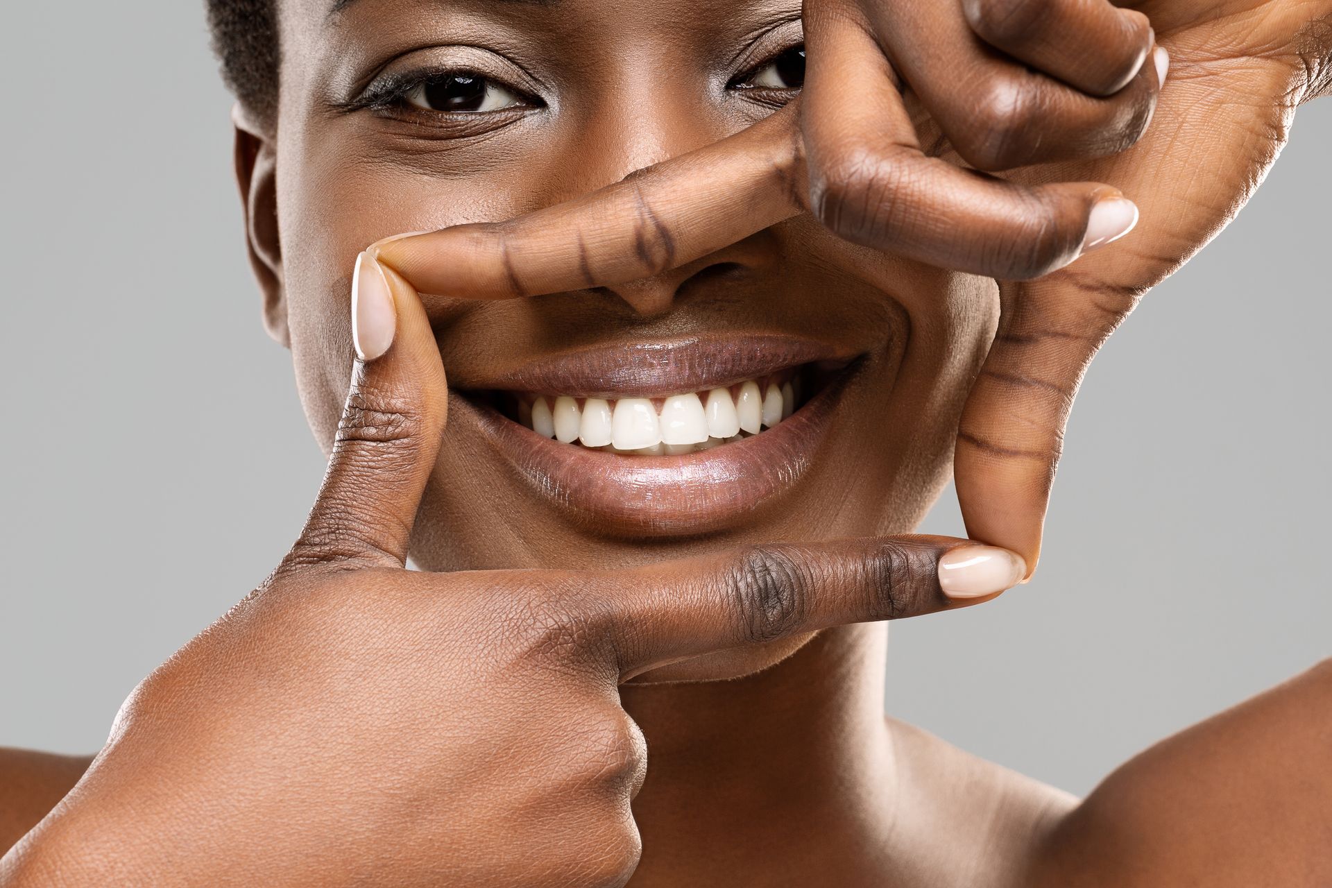 Teen girl smiling with new braces at orthodontist appointment with dental hygienist. Beautiful black woman framing her healthy white teeth with fingers.