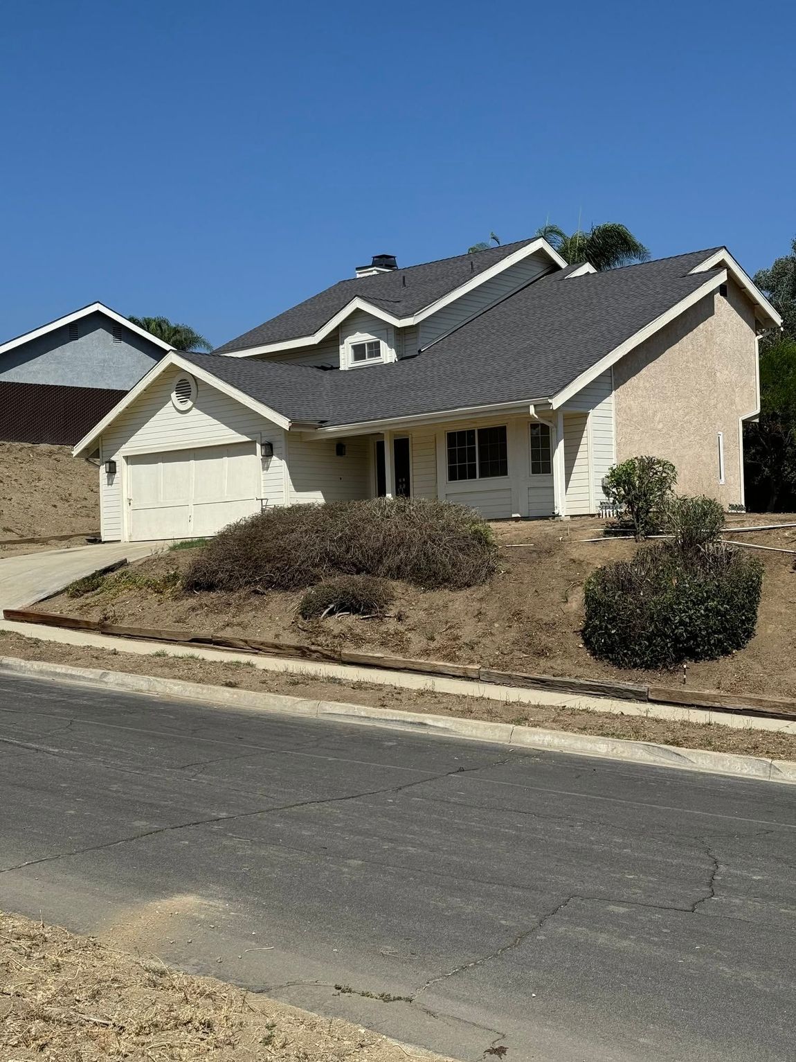 Suburban house with tan brick, gray roof, and a two-car garage beside a curb-lined street