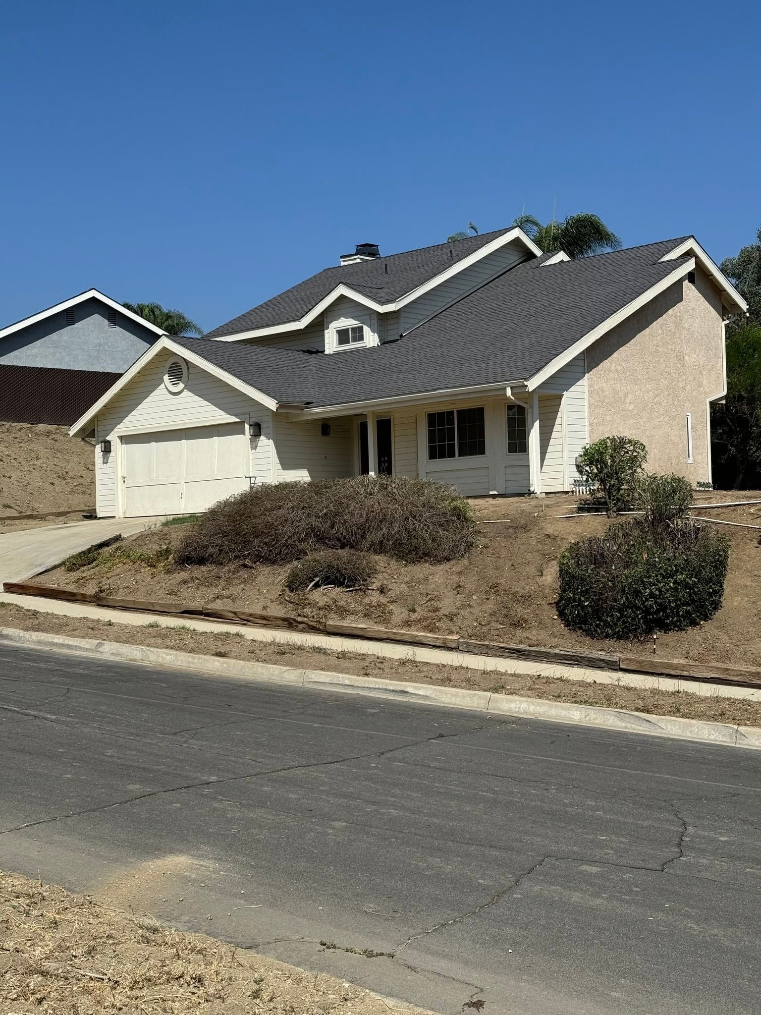 Suburban house with tan brick, gray roof, and a two-car garage beside a curb-lined street