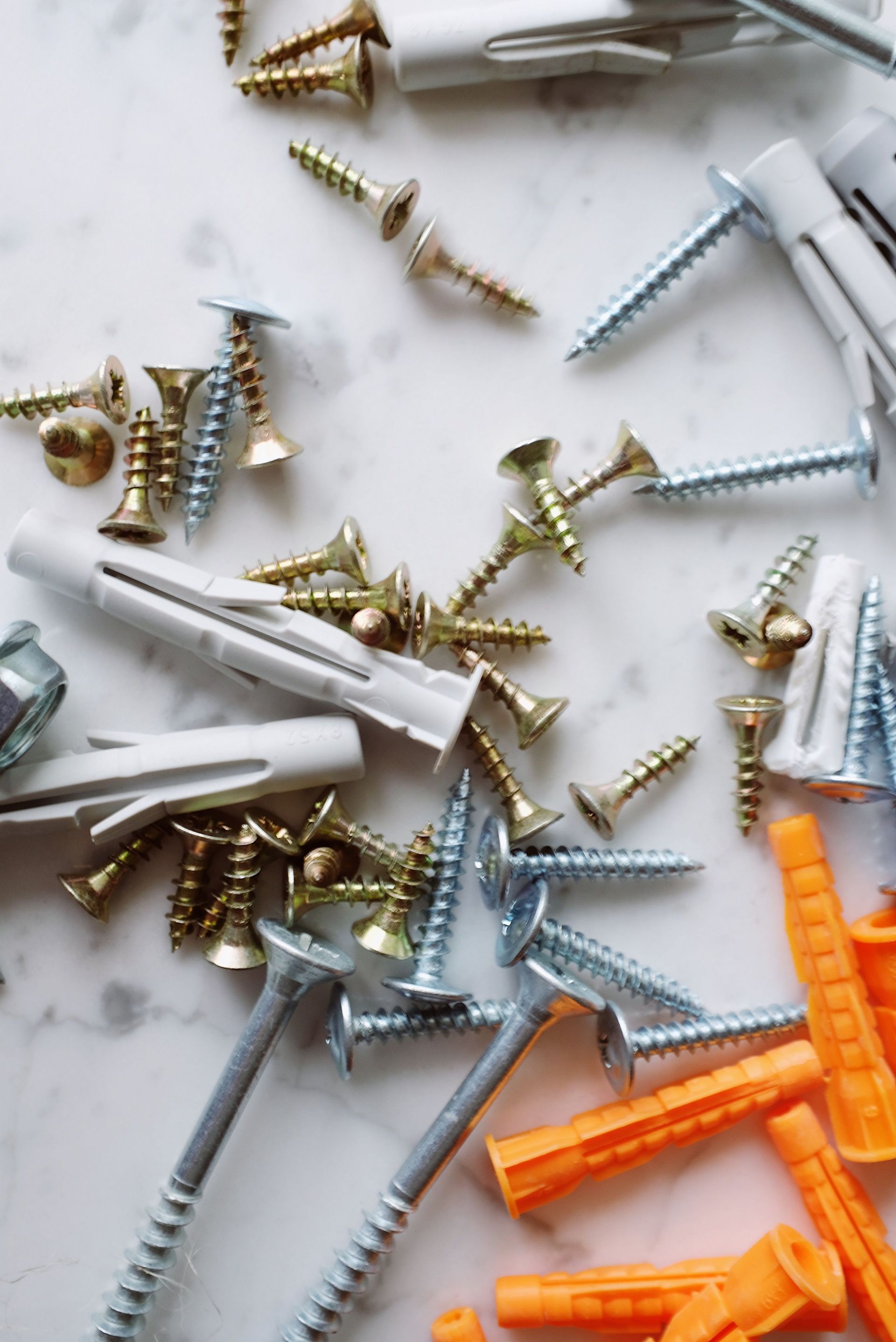 Assorted screws and wall anchors in white, silver, gold, and orange on a plain background