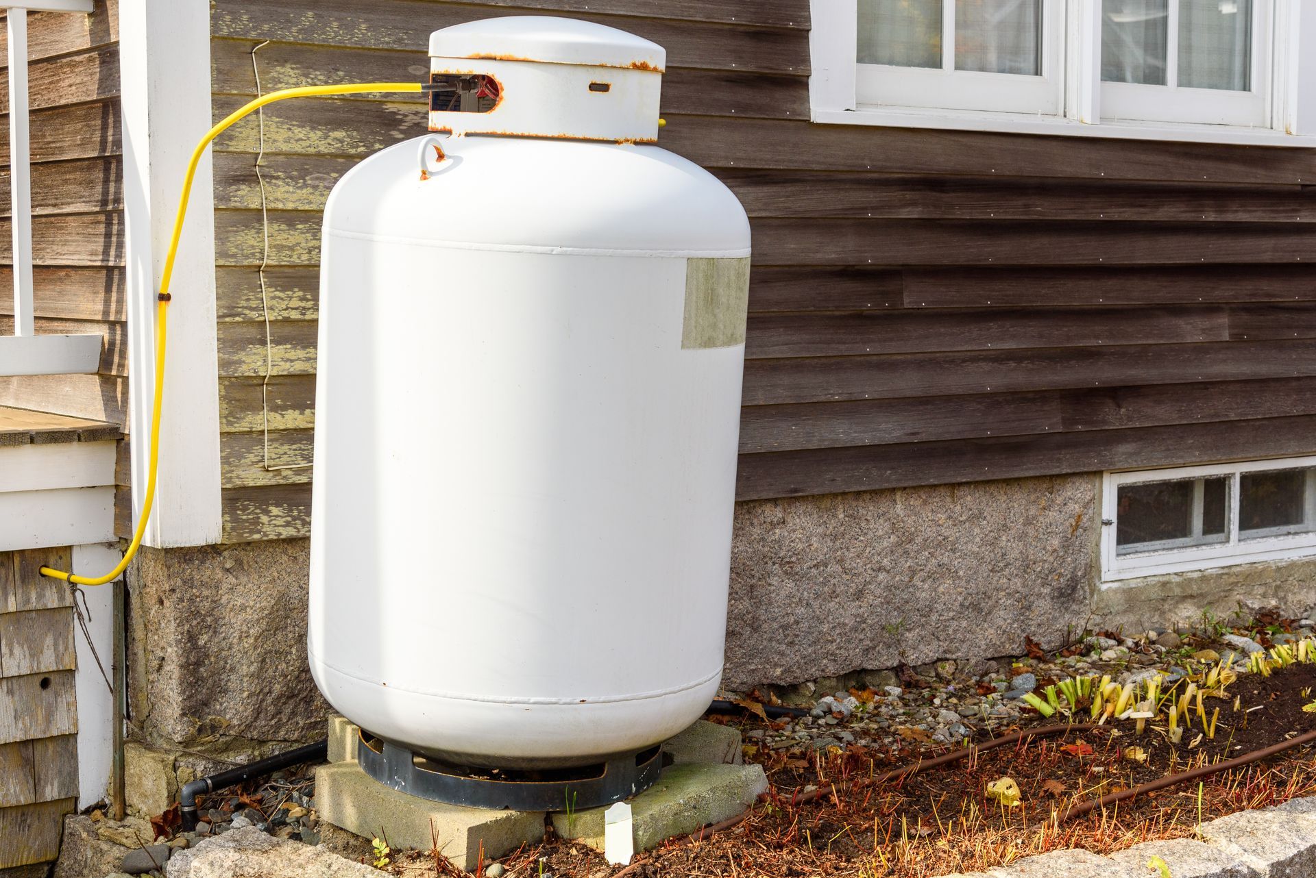 Row of weathered orange propane cylinders loaded on a truck bed from residential propane suppliers. a white propane cylinder against the external wooden wall of a house.