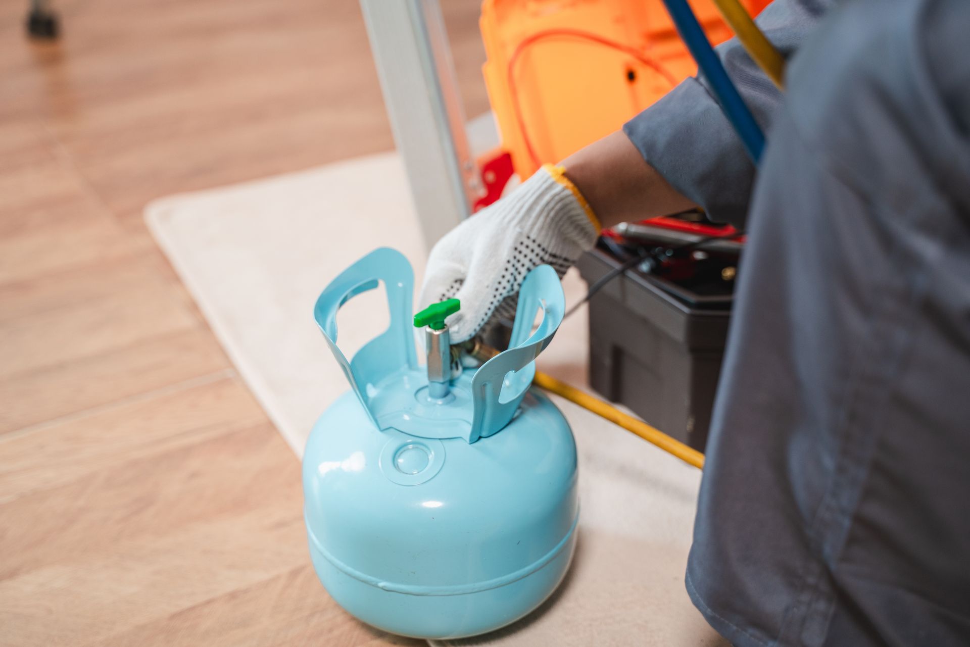 A gloved technician adjusting a valve on a small blue gas cylinder beside a toolbox