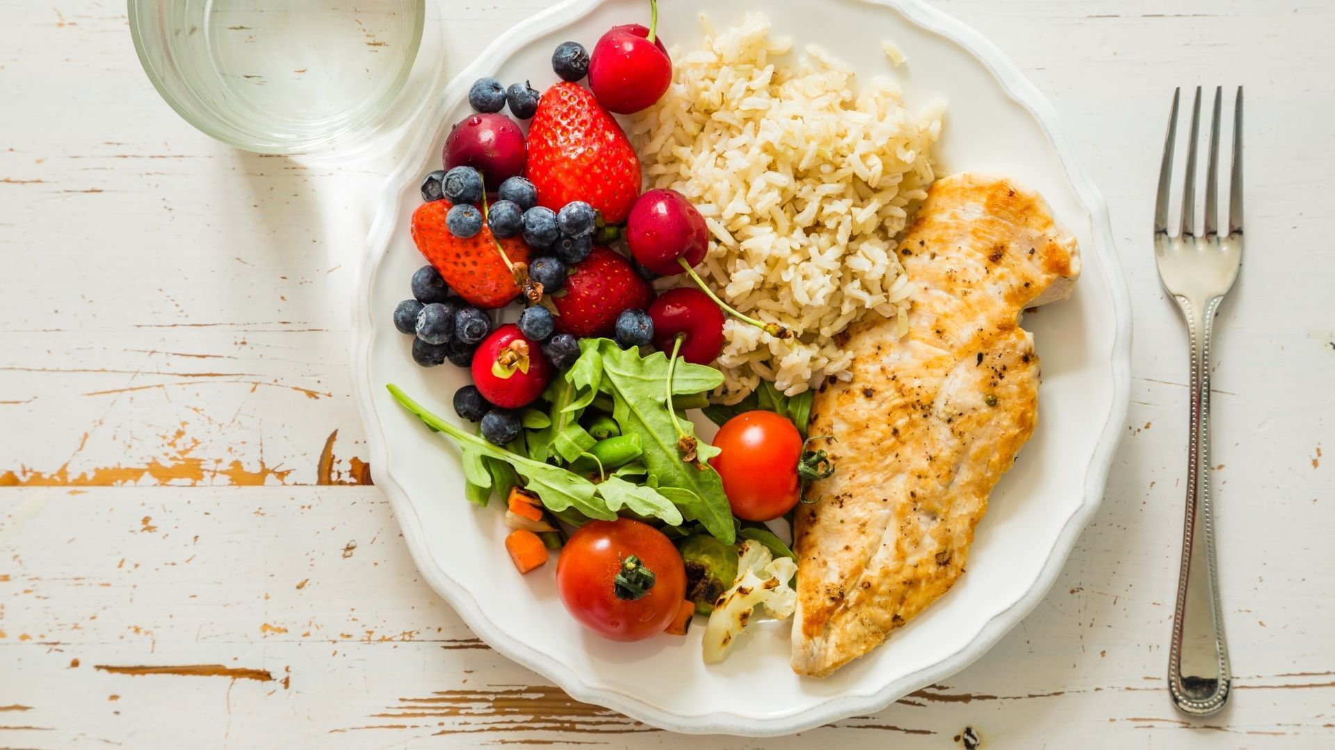 A plate of food with chicken , rice , berries , and a fork on a table.