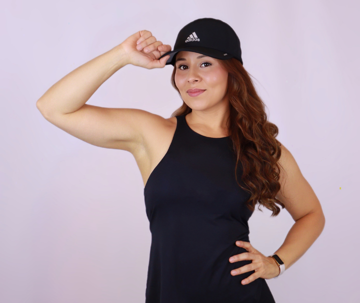 Jess in a black cap and tank top flexing her arm