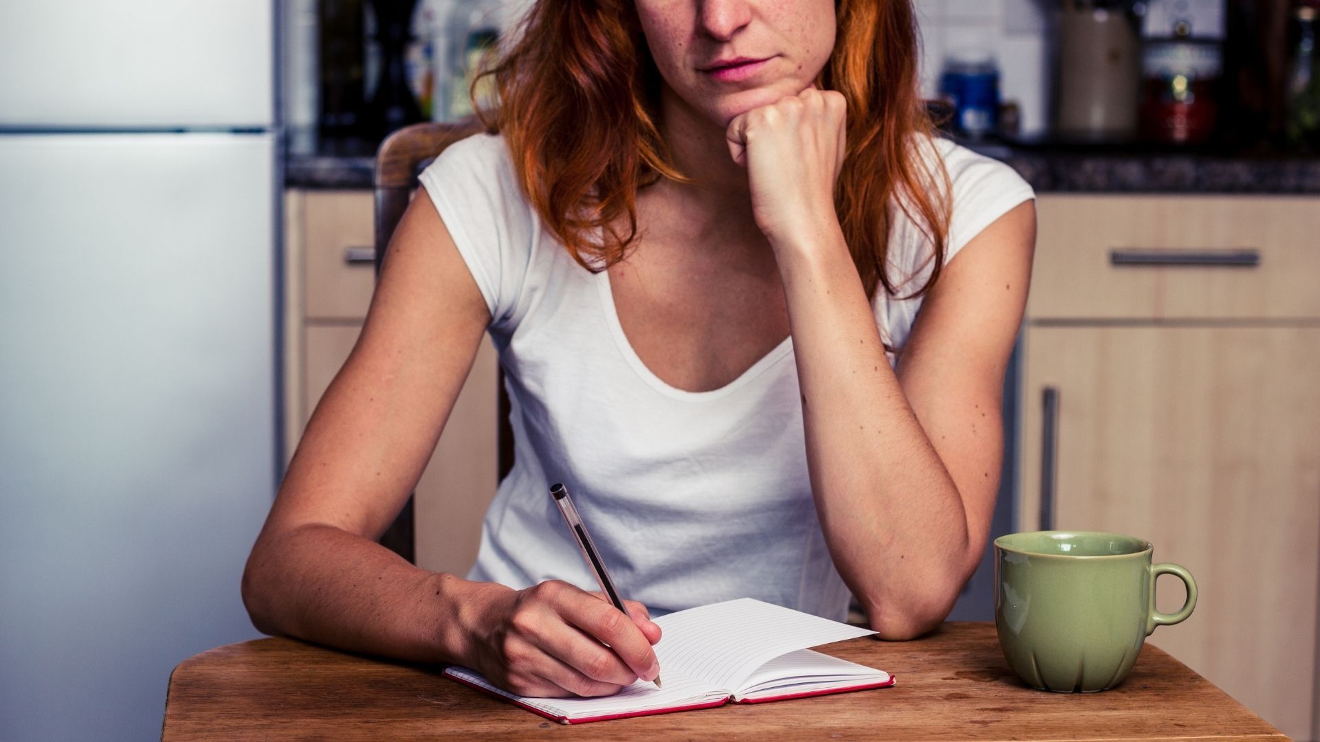 A woman is sitting at a table writing in a notebook.