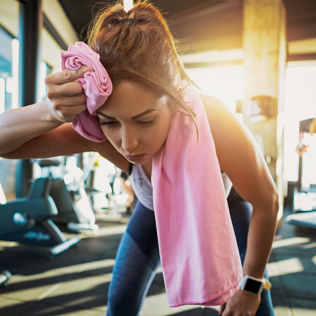 A woman is wiping her forehead with a pink towel in a gym.