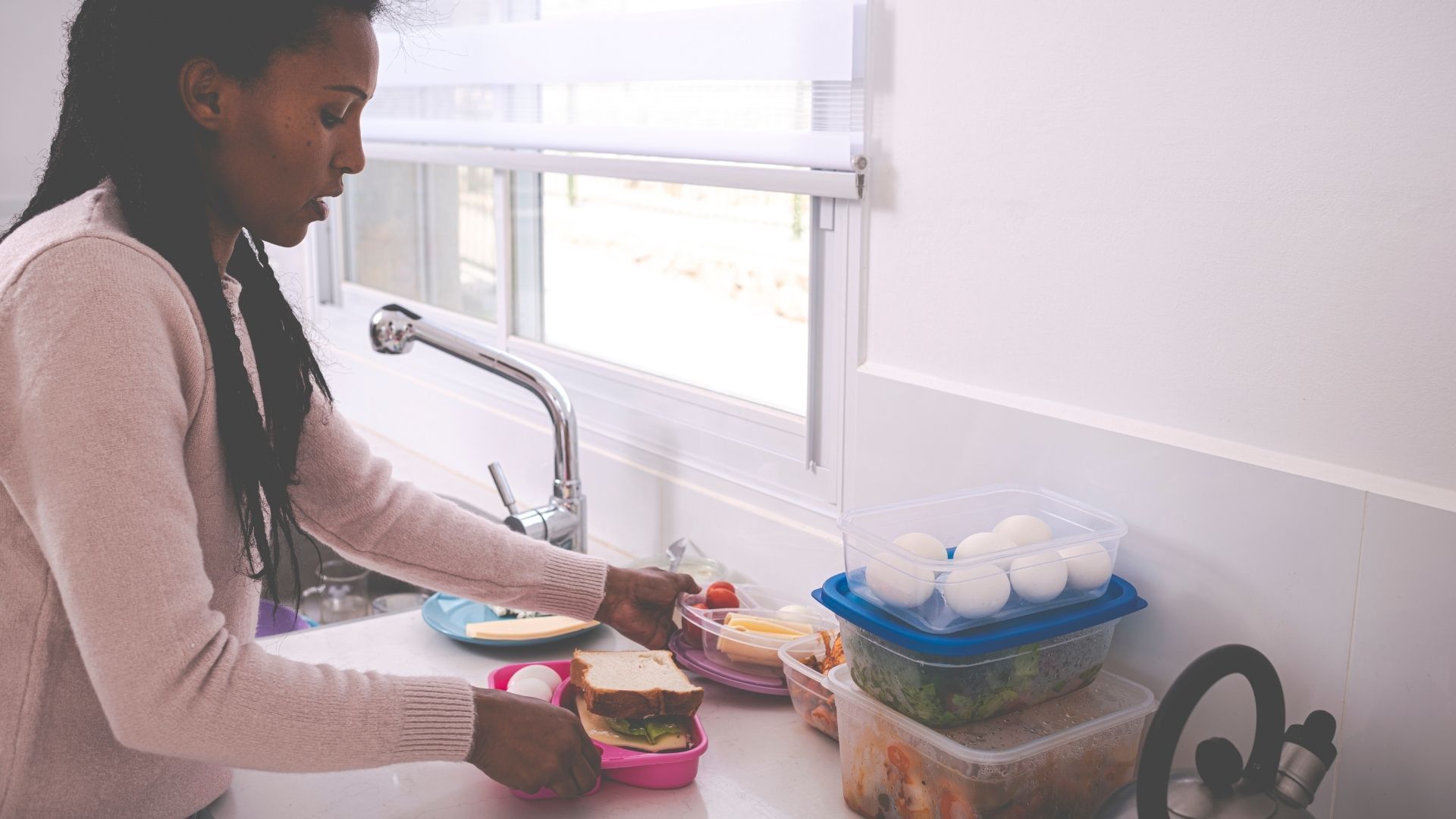 A woman is making a sandwich in a plastic container in a kitchen.