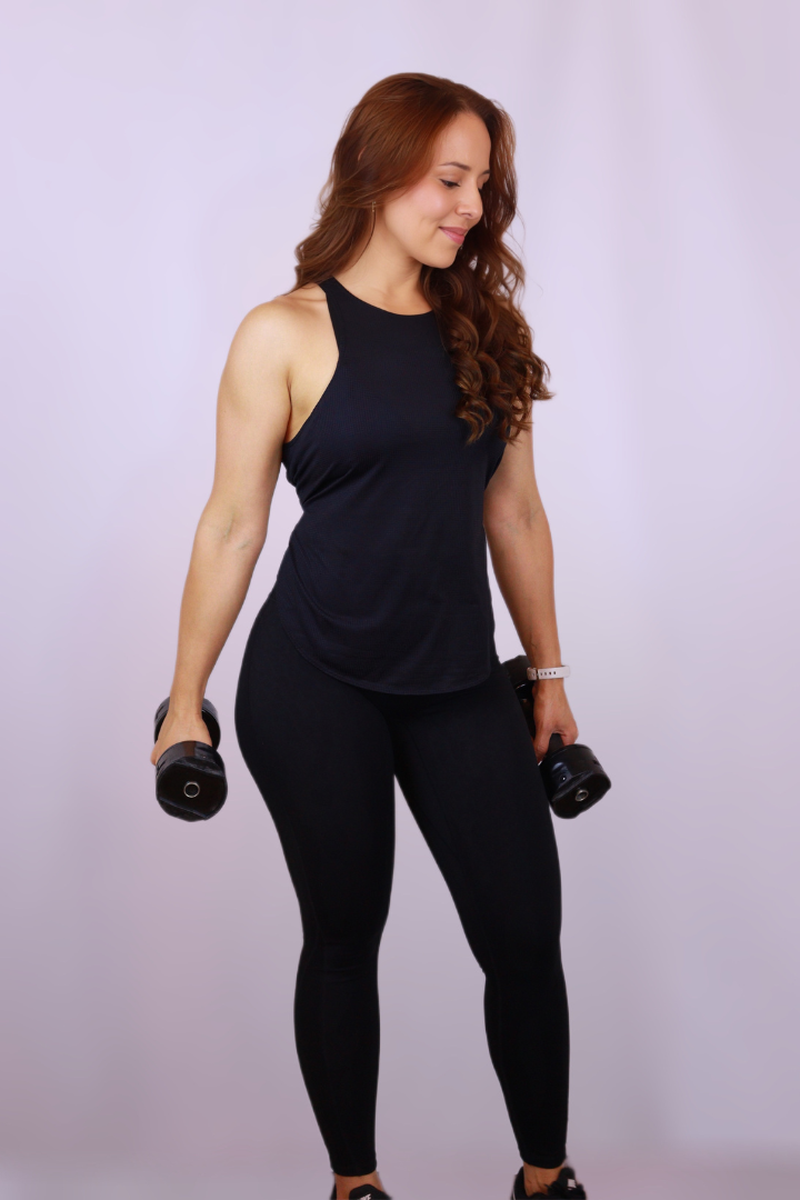 A woman in a black tank top and black leggings is holding two dumbbells.