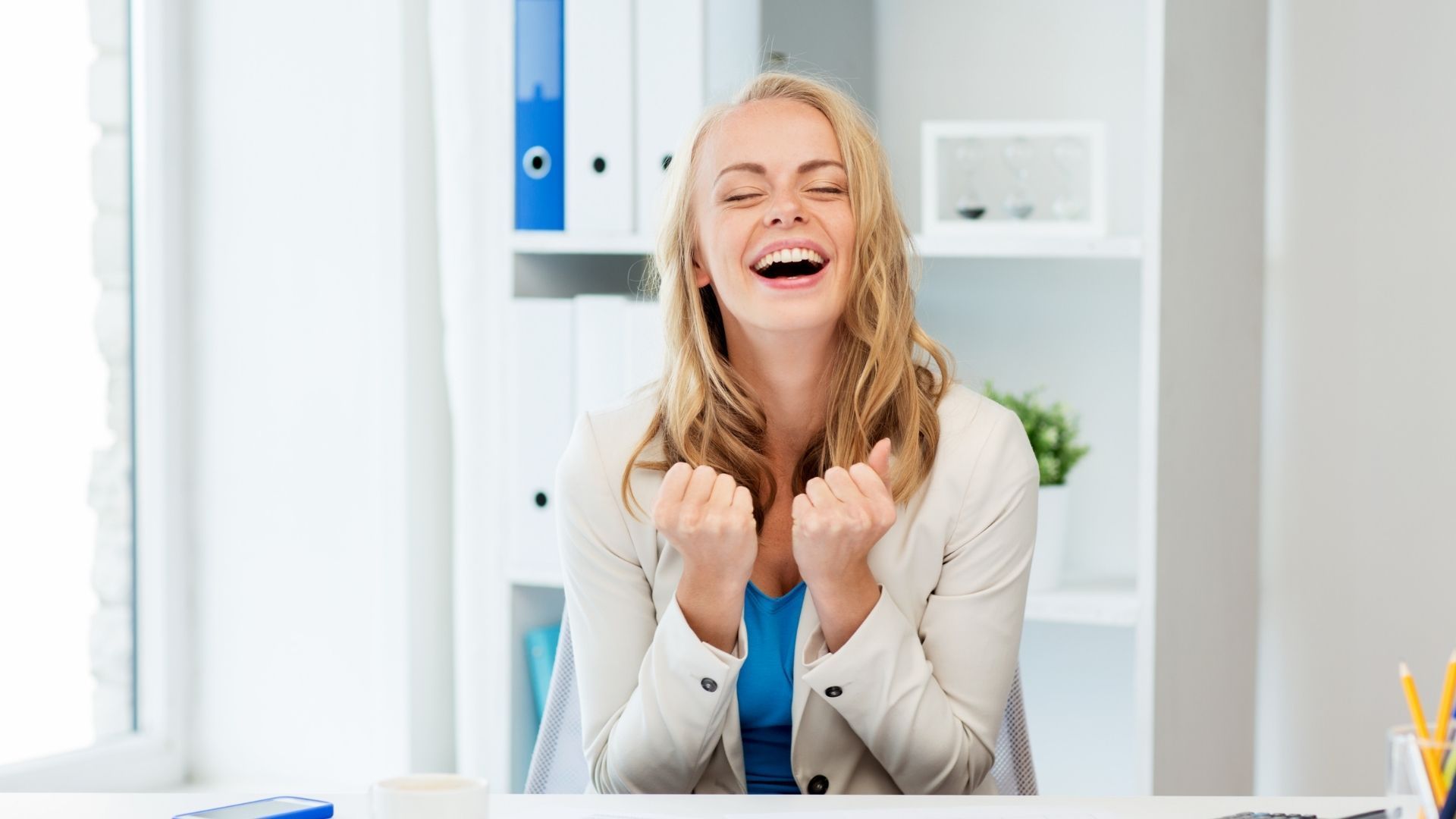 A woman is sitting at a desk with her hands in the air.